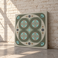 A square canvas print with a retro geometric pattern in muted olive green, beige, light blue, and gray, leaning against a white brick wall on a concrete floor.