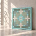 A square canvas wall art print with a geometric pattern in shades of teal, sage green, and cream, leaning against a textured beige wall on a stone floor with soft sunlight and shadows.
